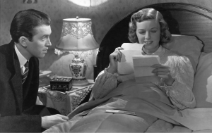 Main leads in the bedroom. Woman reading letters in the bed while man looks at her. 